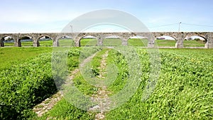 A rural path through a green field and the Aqueduto da Granja aquaduct at Pero Pinheiro