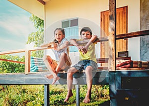 Rural children in Thailand Rural area is sitting in the balcony of a wooden farm house house for Country poverty concept