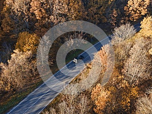 Rural road with black car in yellow and orange autumn fall forest. Aerial view