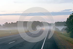 Rural road with headlights of car appearing through the fog