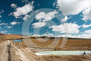 Rural road with mountain river and fishermen under white clouds blue sky