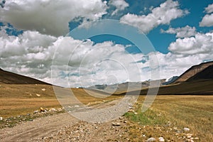 Rural road between the mountains of Central Asia with big clouds in the sky for a moment before a thunderstorm