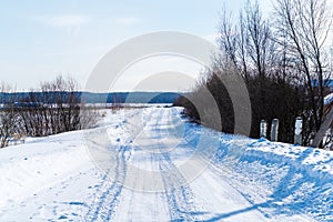 Rural road in winter covered with rolled snow on the background of snow-covered fields and forests with a clear sky