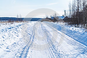 Rural road in winter covered with rolled snow on the background of snow-covered fields and forests with a clear sky