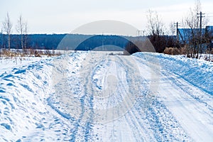 Rural road in winter covered with rolled snow on the background of snow-covered fields and forests with a clear sky