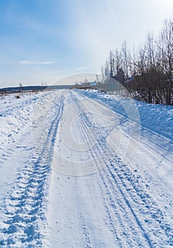 Rural road in winter covered with rolled snow on the background of snow-covered fields and forests with a clear sky