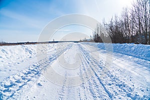 Rural road in winter covered with rolled snow on the background of snow-covered fields and forests with a clear sky