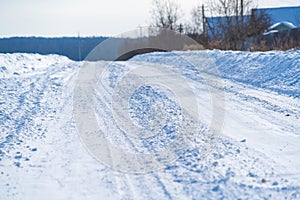 Rural road in winter covered with rolled snow on the background of snow-covered fields and forests with a clear sky