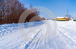 Rural road in winter covered with rolled snow on the background of snow-covered fields and forests with a clear sky