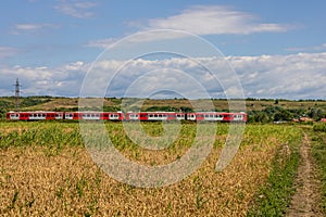 Rural Romanian landscape with a train passing through. The land is a patchwork of wheat and corn fields