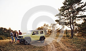 Rural scene. Group of cheerful friends have nice weekend at sunny day near theirs green car outdoors