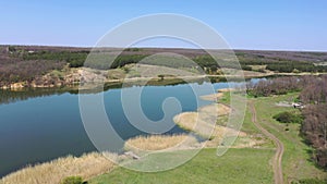 Rural scene in the spring. Lake, country road and forest aerial view