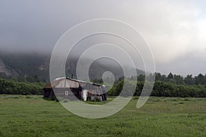 rural simple house in the forest in the morning at the foot of the mountain in a thick fog, gloomy disturbing landscape