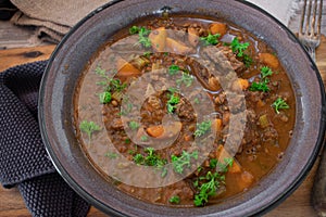 Rural stew in a enamel bowl on wooden table background