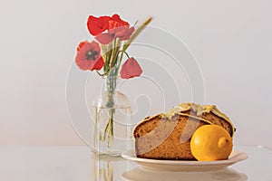 Rural still life with red poppies in glass vase and a plate with biscocho Bizcocho lemon muffin on kitchen table. Sweet photo