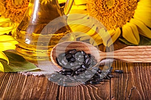 Rural still-life - the sunflower oil in glass cruet with flowers of sunflower Helianthus annuus and seeds in a wooden spoon