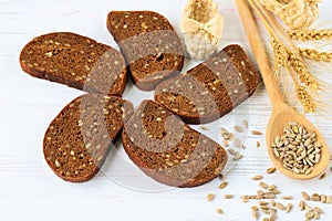 Rural still life on a white wooden background - brown bread, sunflower ,seeds on a light wooden spoon and ears of wheat