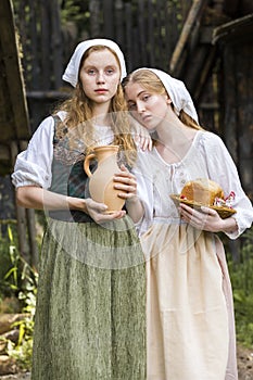 Rural Style Concepts. Pair of Young Beautful Caucasian Girlfriends in Traditional Rural Outfit  Posing With Caly Jar And Bread