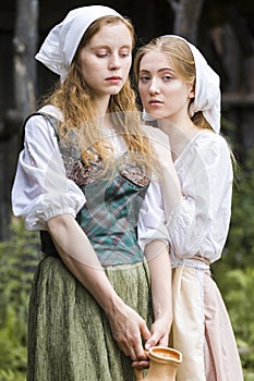 Rural Style Concepts. Two Young Beautful Caucasian Girlfriends in Traditional Rural Outfit  Posing With Caly Jar And Bread