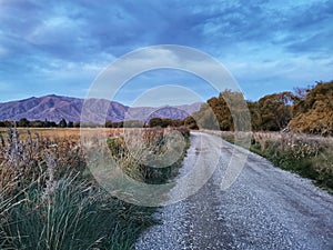 A rural unsealed road with cloudy sky and mountains on the background