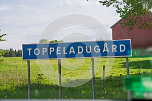 A rural village name sign with the name Toppeladugård mounted next to green pasture and barn in rural Skåne Sweden