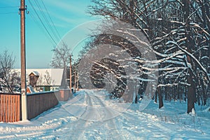 Country road covered with snow between houses and woods