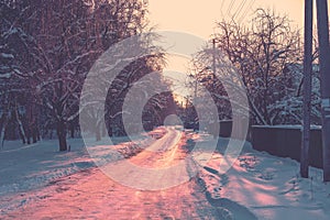 Country road covered with snow between houses and woods