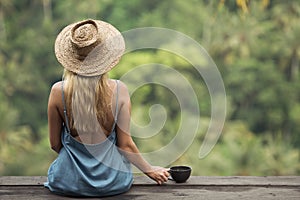 Rural woman with cup of coffee siting and look on jungle.