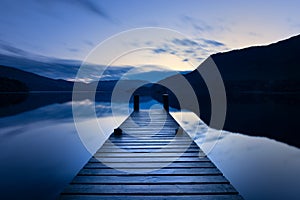 Wooden Jetty/Pier Leading Out To Calm Lake With Reflections At Blue Hour In The Lake District, UK