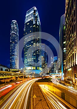 Rush hour traffic light trails lead to tall vertical skyscrapers in Hong Kong downtown