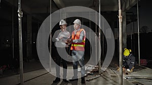 In rush work overtime, engineers and architects are consulting on a construction site with construction workers grinding steel in