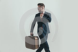 Rushed businessman with baggage fixing tie and looking over shoulder photo