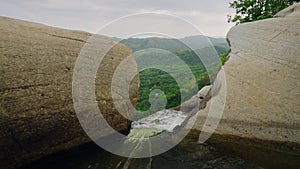 Rushing water flows from river into waterfall over rocks, green hills surround area. Clear view of nature, waterfalls in