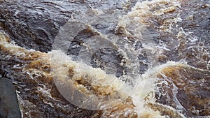 Rushing water in the river, top view. Dark ferrous water rushes in the stream. A yellow-white foam. Karelia, Lososinka