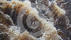 Rushing water in the river, top view. Water rushes in the stream. A yellow-white foam. Karelia, Lososinka River in