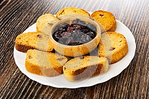 Rusks with raisin, dried grape in bowl on plate on wooden table