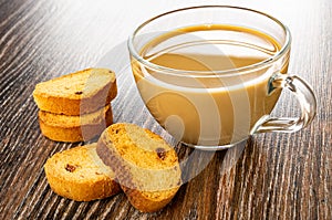 Rusks with raisin, transparent cup of coffee with milk on wooden table