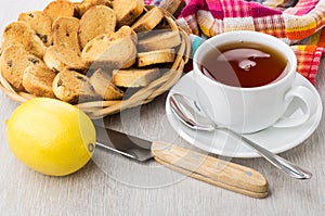 Rusks with raisin in wicker basket, tea, lemon, knife