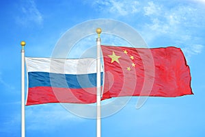 Russia and China two flags on flagpoles and blue cloudy sky