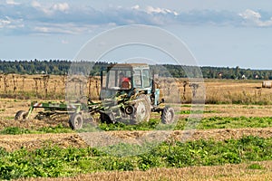 Russia. Gatchinsky district of the Leningrad region. August 28, 2021. The tractor puts hay on the field in the tracks