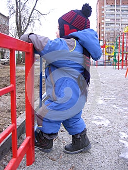 Russia,  a small child boy walks on the street in autumn climbs over the fence