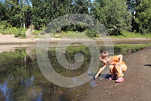 a small child plays in the water with ducks in a pond in nature in summer