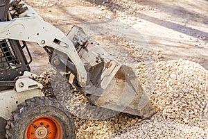 Utility tractor Mini loader Bobcat S175 rakes gravel during repair of asphalt on a city street