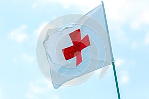 Flag with a red cross develops against a blue sky. Red Cross emblem of the international Red Cross, international humanitarian org