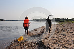 Russia, a small child boy on the river in a life jacket with a dog swims with a toy