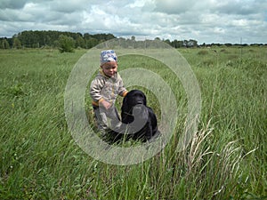 Russia,  a small child hugs and strokes a large black dog in the grass