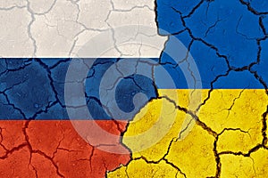 Russia vs Ukraine national flags grunge pattern on grungy dry cracking parched earth. Cracked soil