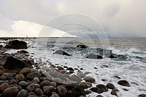 Russian Arctic View, North. Sky with clouds and blue sky reflection in water with waves and snow mountains background with stones