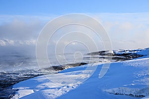 Russian Arctic View, North. Sky with clouds and blue sky reflection in water with waves and snow mountains background with stones