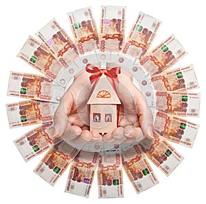 Russian banknotes are arranged in a circle in the center of the hand holding a paper house with a red bow.